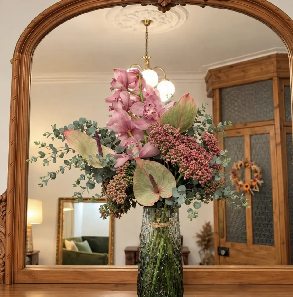 Pink orchid, anthurium and eucalyptus arrangement in a green glass vase