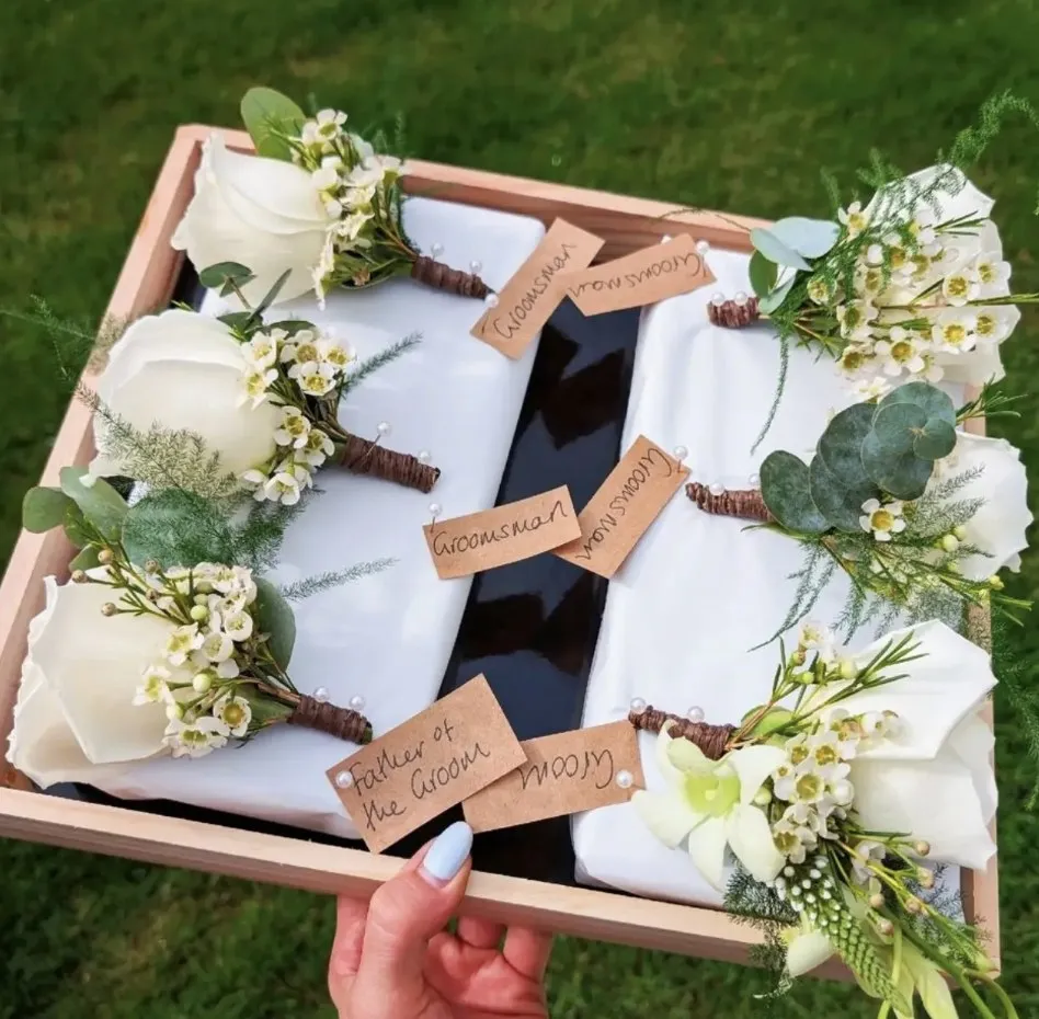Tray of white rose buttonholes labelled for the groomsmen